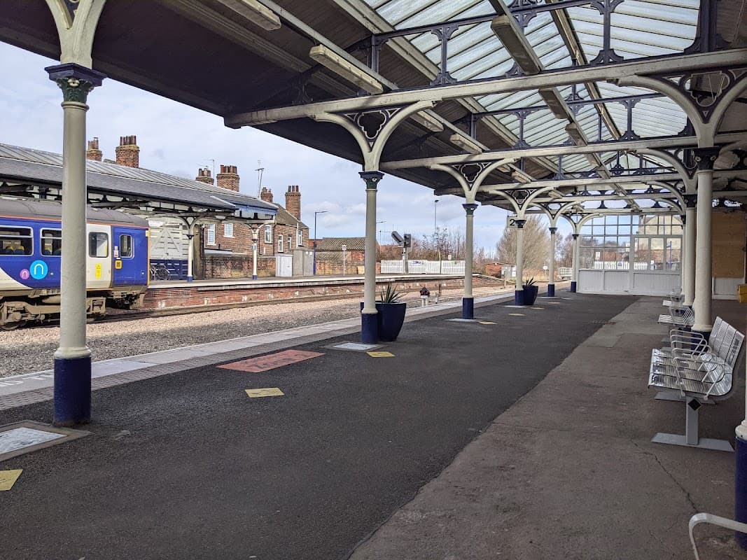 Railway platform at Selby Station with benches, planters, and a train approaching in the background.