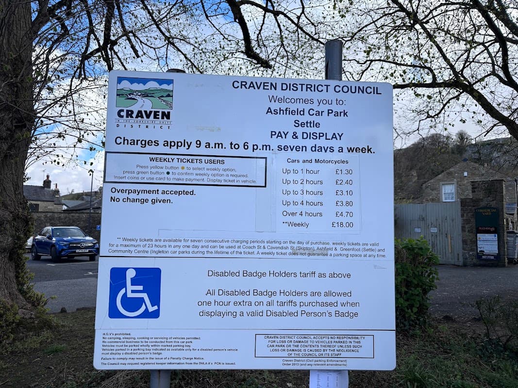 Sign detailing parking charges and regulations at Ashfield Car Park, Settle, with information on disabled badge holders.