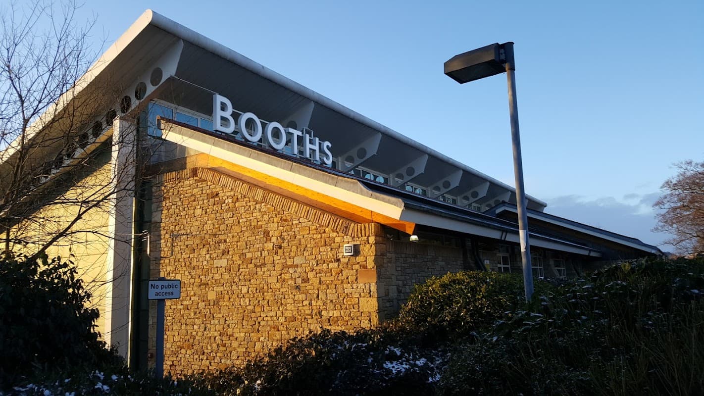 Modern building with a stone facade, large windows, and a prominent sign reading "Booths" against a clear sky.
