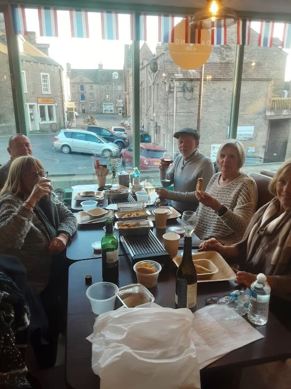 Group of diners enjoying a meal at Darlings of Settle, with drinks and food on the table, in a cozy restaurant setting.