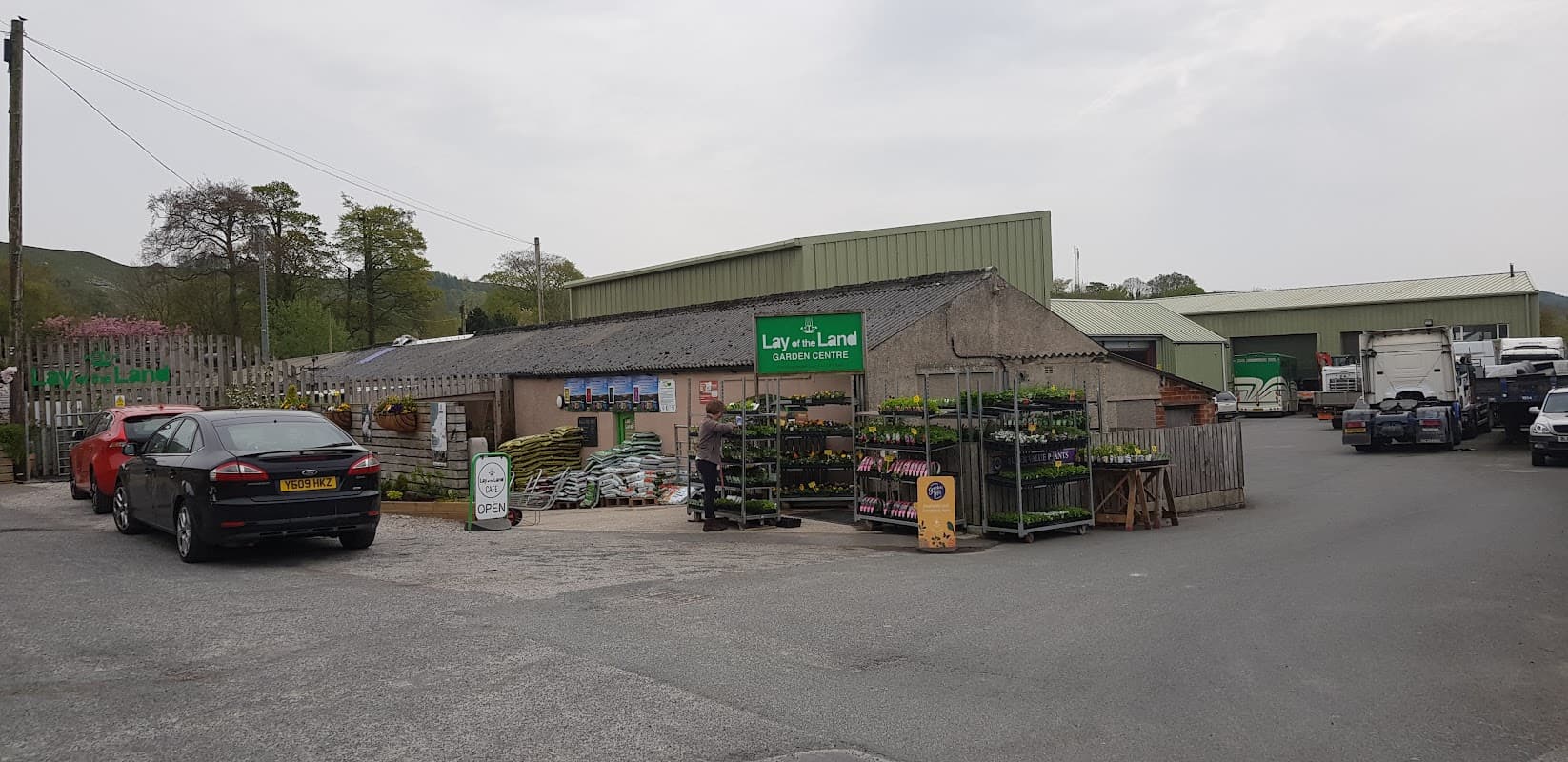 Garden centre with a café, featuring a gravel parking area, plant displays, and green signage in Settle, Yorkshire.