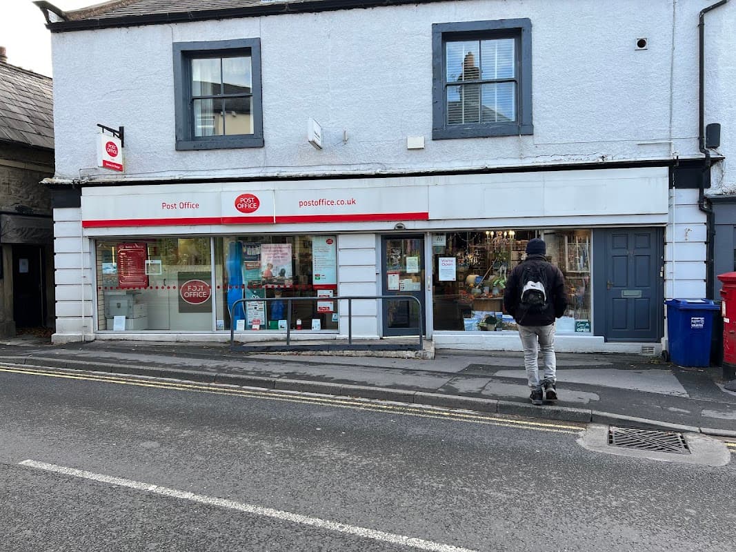 Settle Post Office with a red and white sign, large windows, and a person walking by on a quiet street.