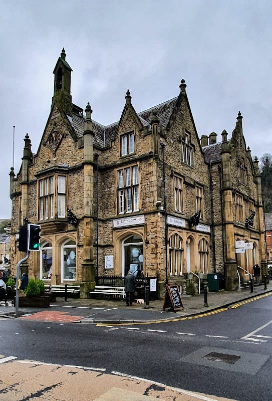 Victorian-style building with stone faΓ§ade, decorative gables, and signage for bathrooms, set in a town square.