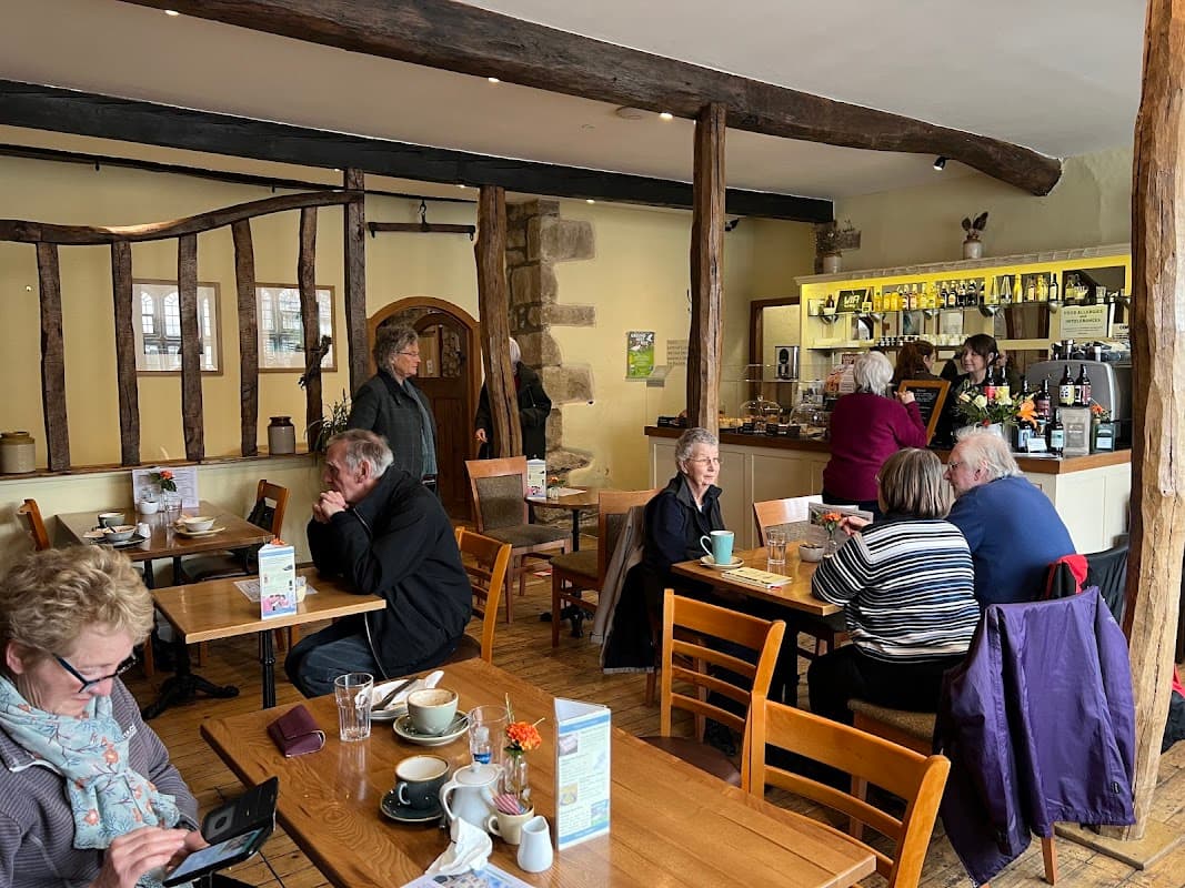 Cozy café interior with wooden beams, patrons enjoying coffee, and a barista serving at the counter.