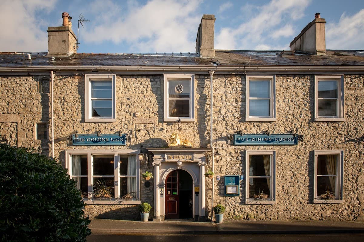 Charming stone building with a golden lion sign, blue window frames, and a welcoming entrance in Settle, Yorkshire.