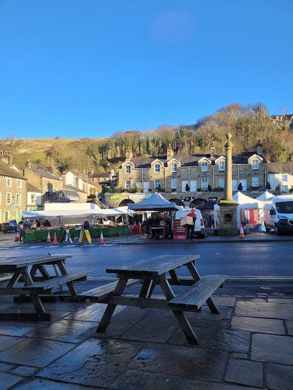 Quaint café with outdoor seating, market stalls, and historic buildings under a clear blue sky in Settle, Yorkshire.