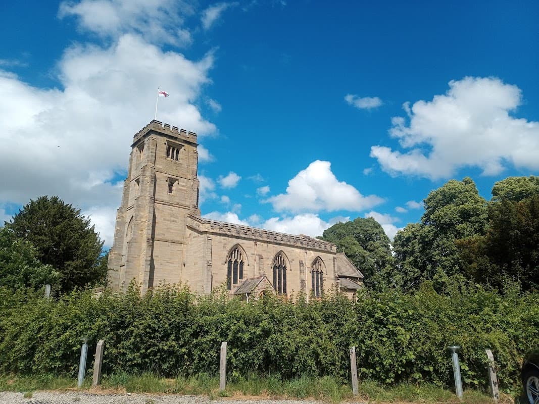 Historic stone church with a tall tower, surrounded by lush greenery and a bright blue sky with fluffy clouds.