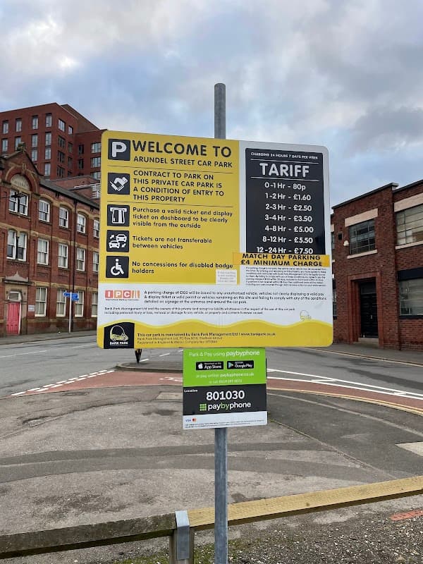 Sign for Arundel Street Car Park detailing parking tariffs and conditions, with nearby buildings in the background.
