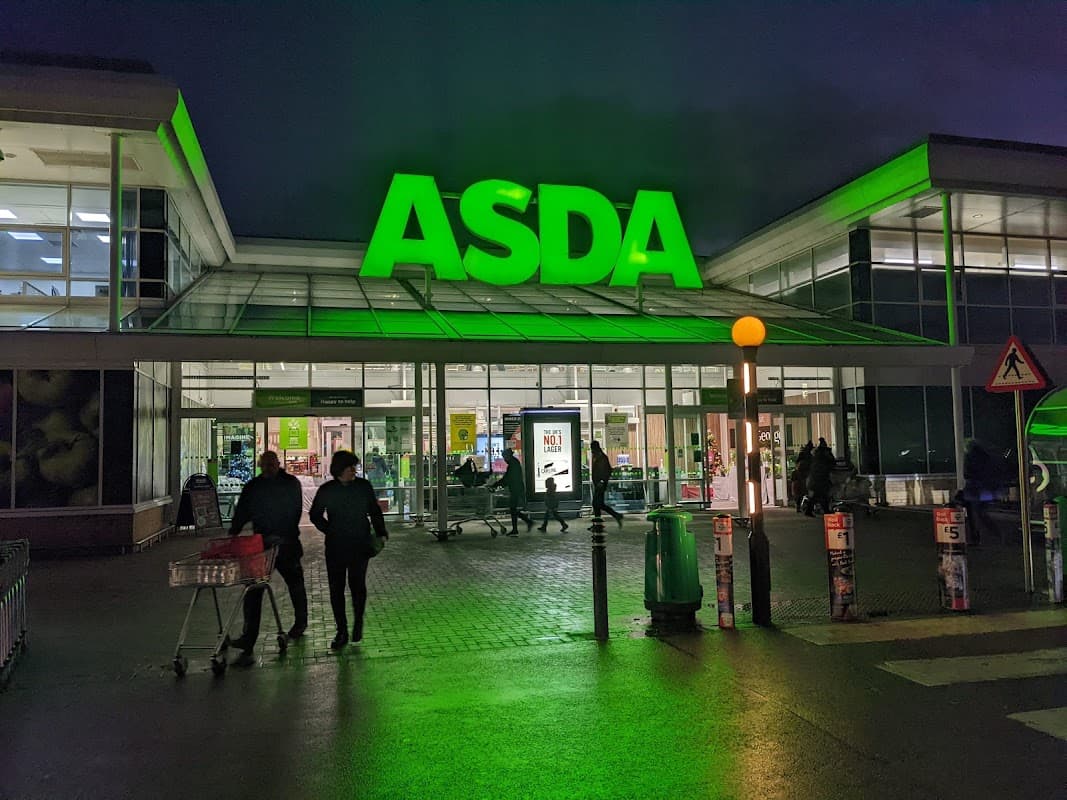 Bright green "ASDA" sign illuminated at night, with shoppers entering and exiting the Sheffield Supercentre.