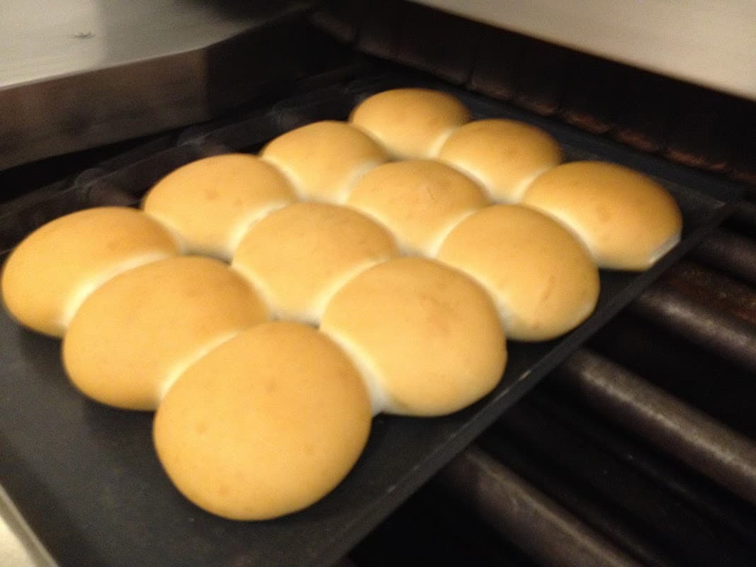 Freshly baked golden rolls arranged neatly on a tray, with a baking oven in the background.