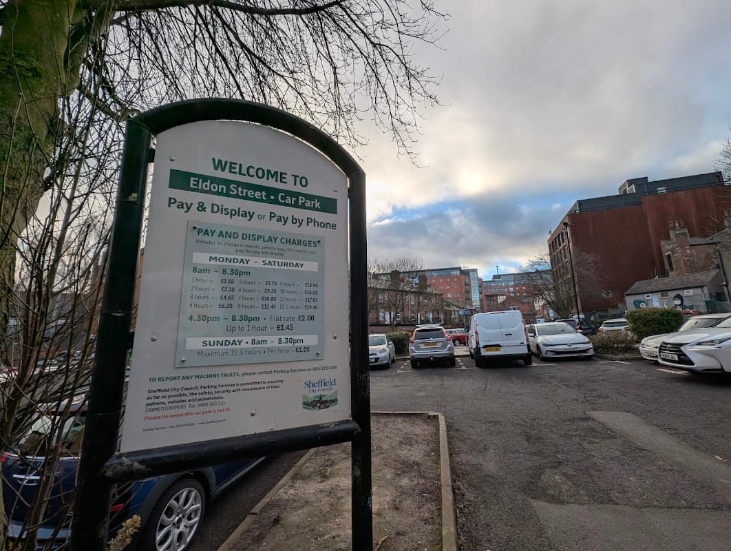 Welcome sign for Eldon Street Car Park with parking fees and hours, surrounded by parked cars and a cloudy sky.