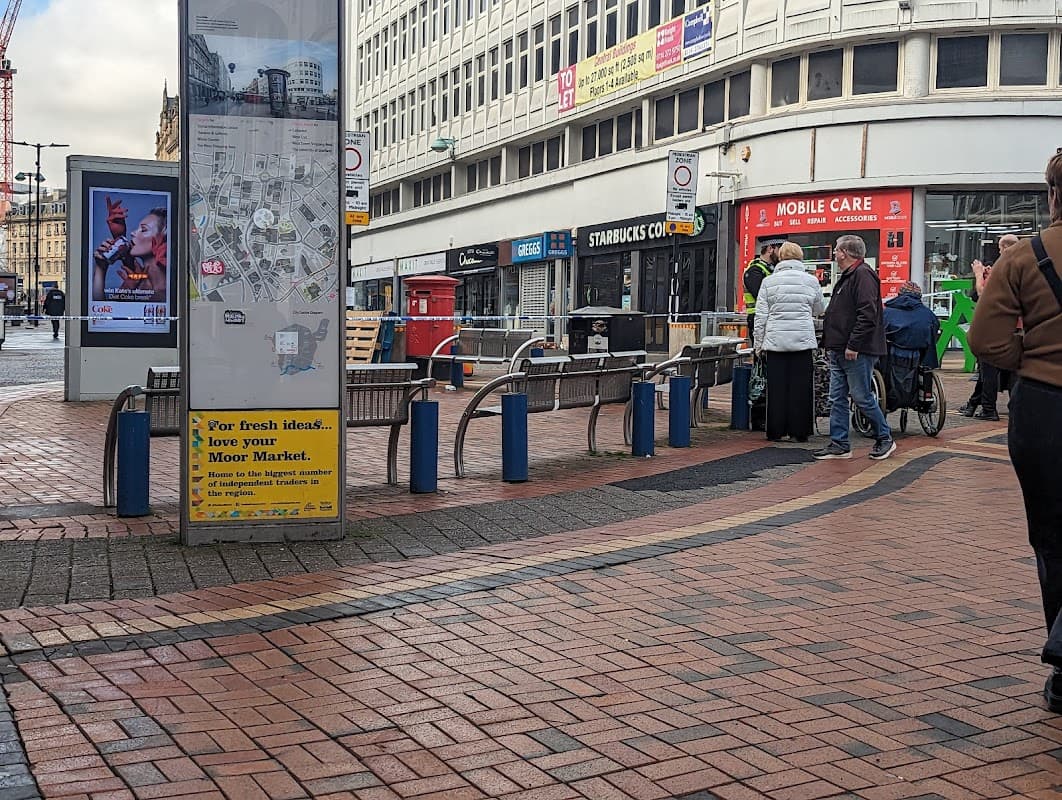Shopping area with a map display, benches, people walking, and nearby storefronts in Sheffield, Yorkshire.