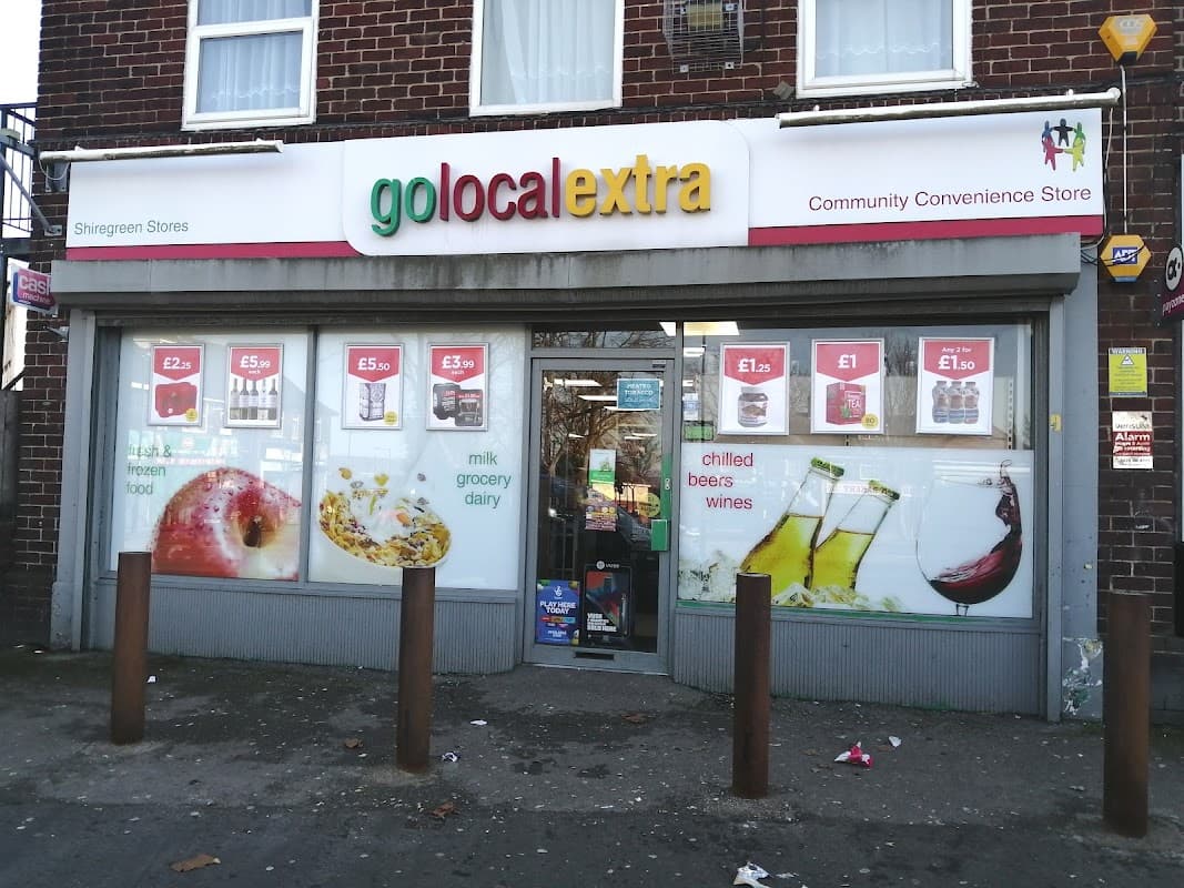 Brightly colored storefront with "Go Local Extra" sign, displaying groceries, drinks, and promotional prices on windows.