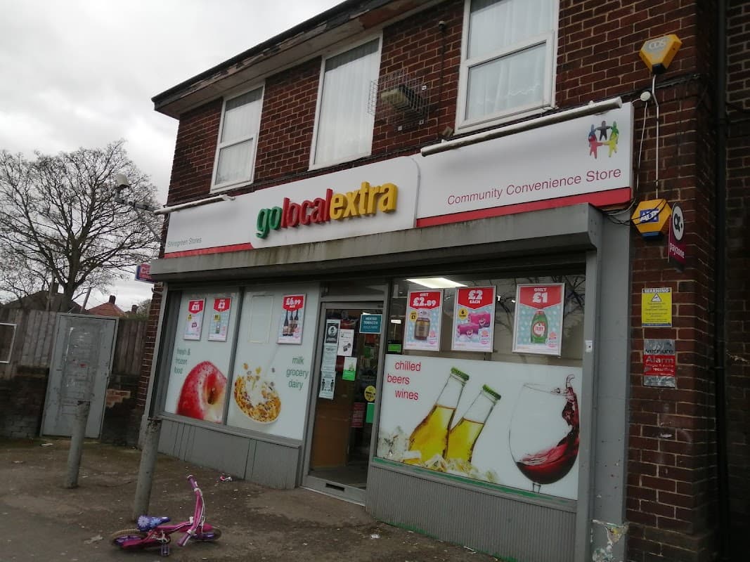 Community convenience store with colorful signage, displaying drinks and snacks, and a pink child's bike outside.