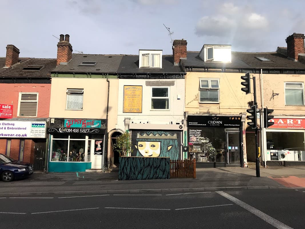 Colorful storefronts along a street, featuring "Gravel Pit Shop" with a mural and nearby businesses in Sheffield.