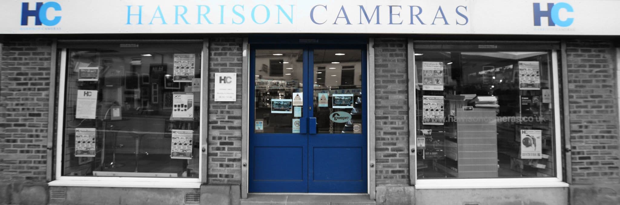 Storefront of Harrison Cameras featuring large windows, blue door, and signage in a brick building.