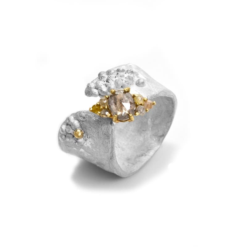 Unique silver ring with textured design and a central golden stone, showcasing a blend of elegance and artistry.