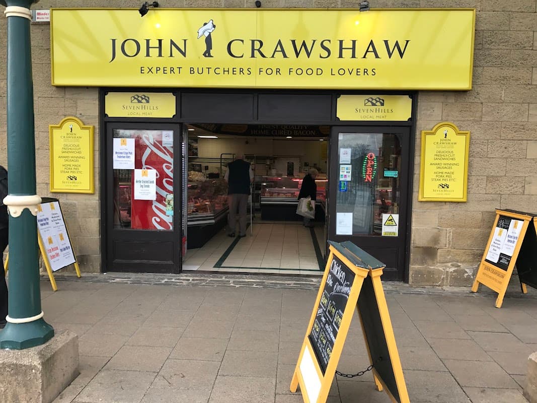 Bright yellow signage for John Crawshaw's Butchers, showcasing meat products, with customers inside and A-frames outside.
