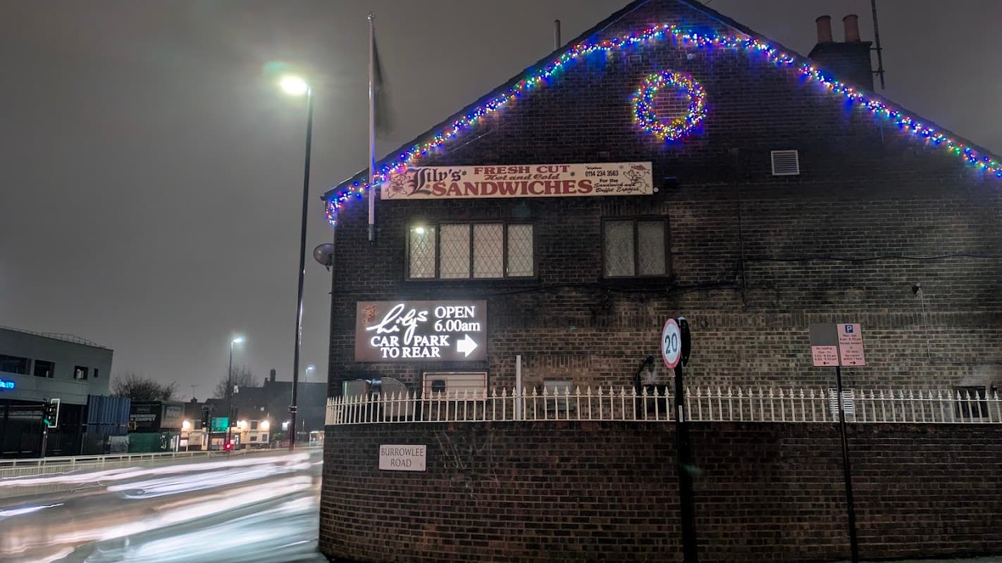 Lily's bakery with festive lights, a sign for fresh sandwiches, and a display indicating hours of operation.