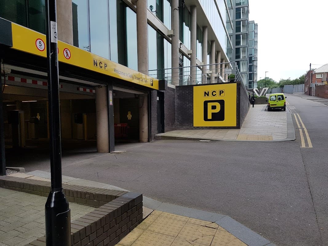 Multi-storey car park entrance with NCP signage, yellow accents, and a green vehicle parked nearby.