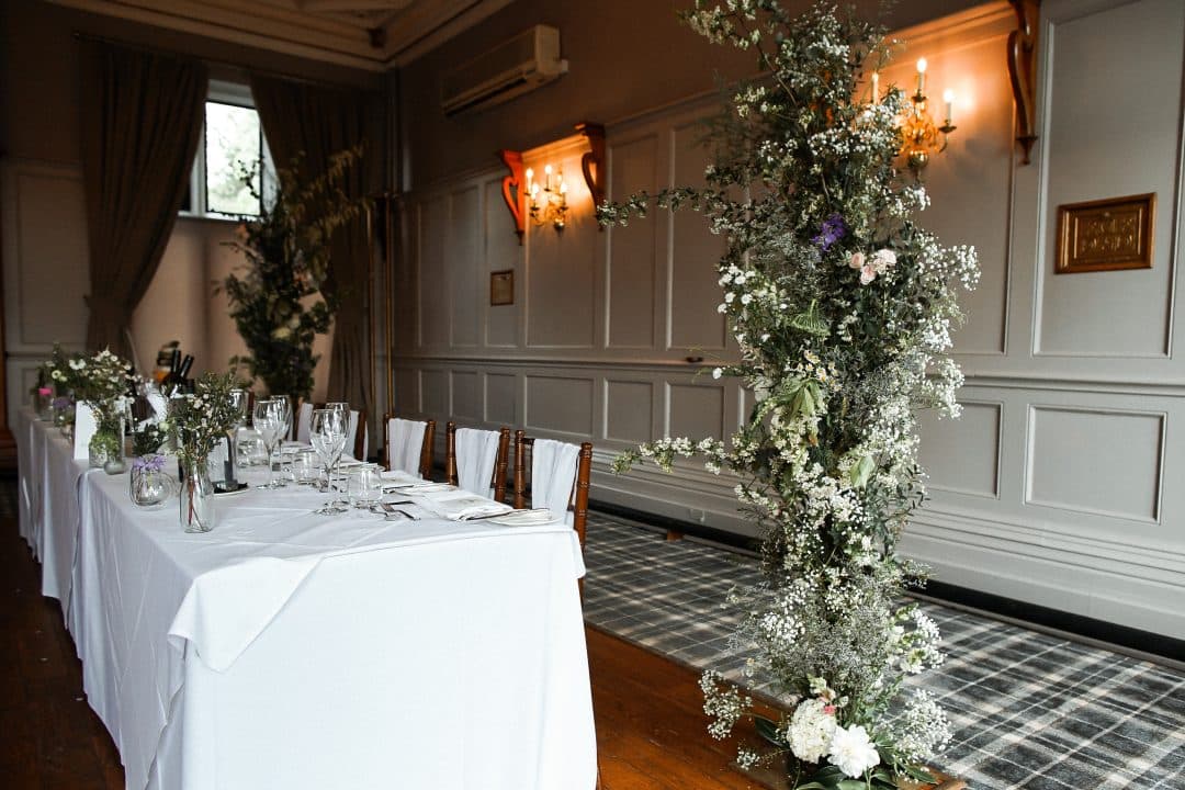 Elegant floral arrangements adorn a beautifully set dining table in a stylish venue with soft lighting and wooden floors.