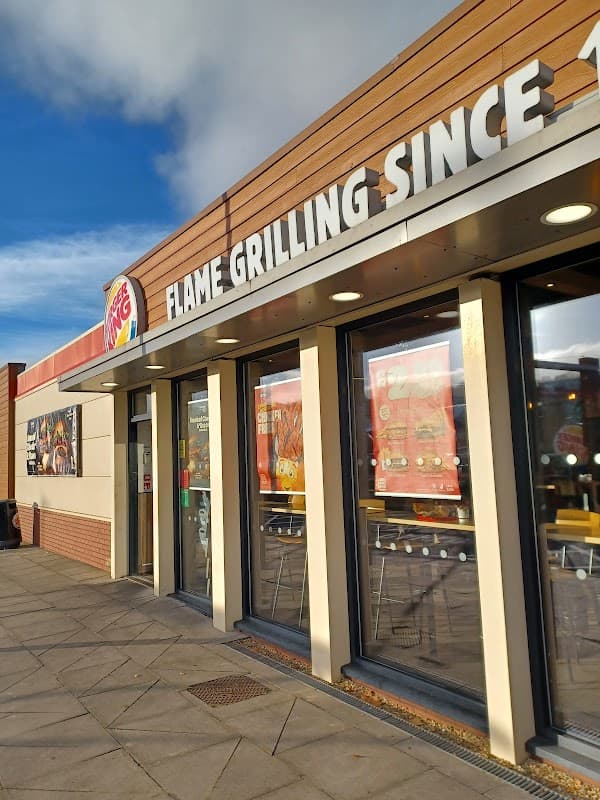Burger King storefront with large windows, showcasing the sign "FLAME GRILLING SINCE" against a blue sky.