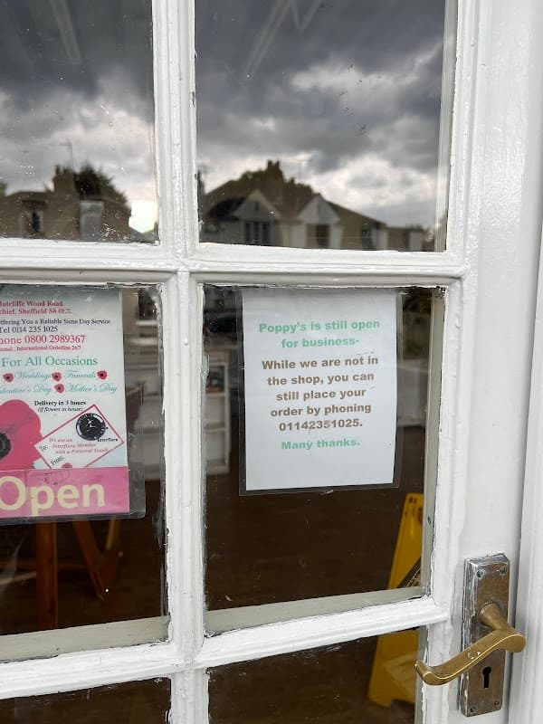 "Window of Poppy's Florist with a sign stating it's open for business and a phone number for orders."