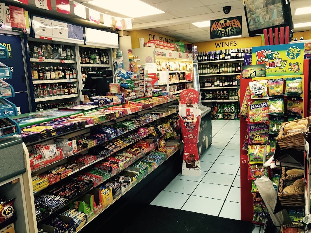 Interior of a convenience store with shelves stocked with snacks, drinks, and wine, featuring colorful candy displays.