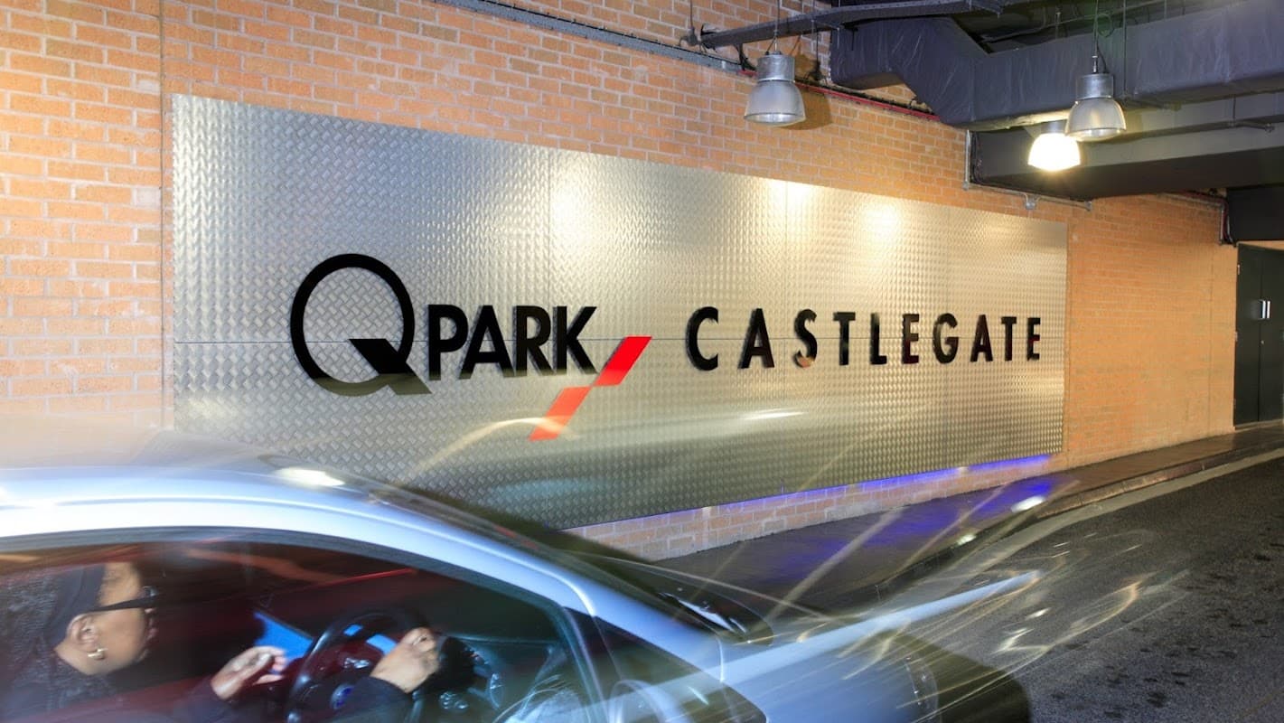 Q-Park Castlegate sign on a brick wall, with a car entering the parking area.