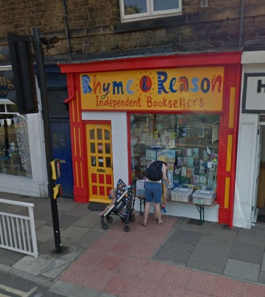 Brightly painted storefront of Rhyme & Reason bookshop with colorful signage, featuring a display of books and a family outside.