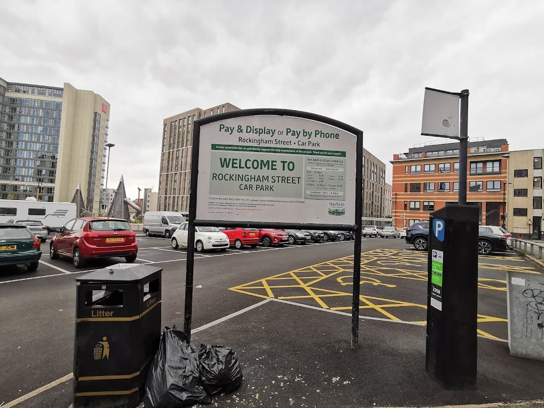 Sign for Rockingham Street Car Park with payment instructions, surrounded by buildings and parking spaces.