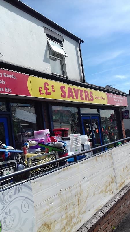 Bright red sign reading "SAVERS Home Store" above a storefront with various household goods displayed outside.