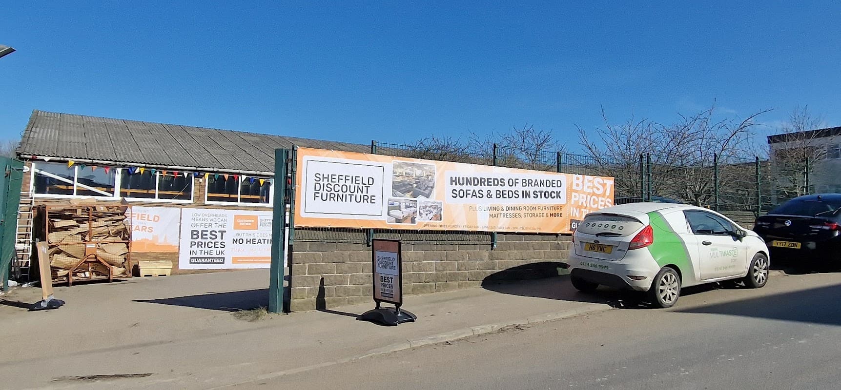 Signage for Sheffield Discount Furniture Store with promotional banners and parked car outside a retail location.