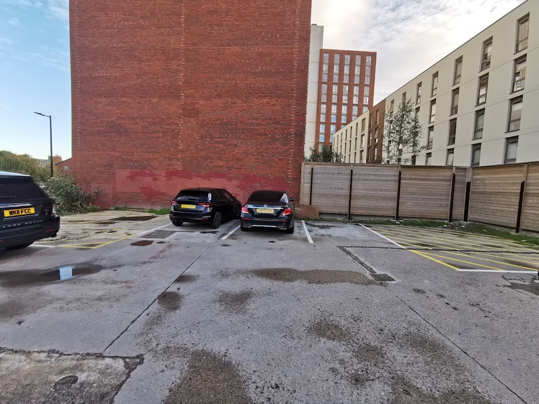 Pay & Display parking area with two parked cars, surrounded by brick buildings and a wooden fence.