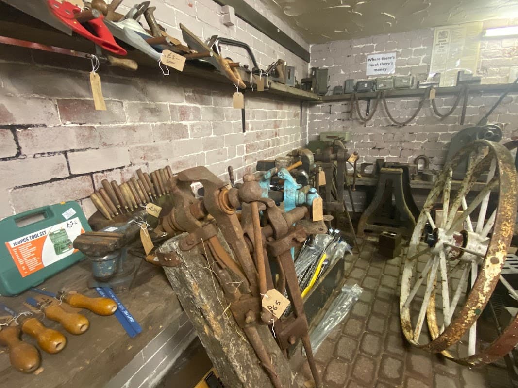 Vintage tools and machinery displayed on wooden shelves in a brick-walled shop, with various items tagged for sale.