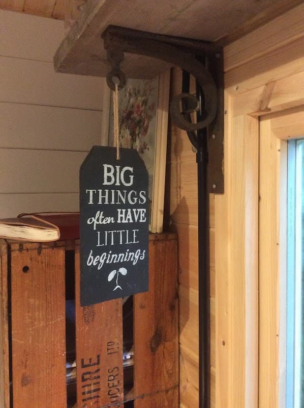 Chalkboard sign reading "BIG THINGS often HAVE little beginnings" hangs from a rustic shelf in a cozy flower shop.