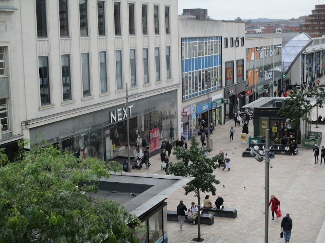 Shopping center with various stores, pedestrians, and greenery; modern architecture and a busy atmosphere in Sheffield.