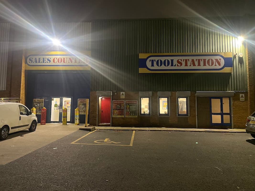 Toolstation storefront at night, featuring bright signage and a sales counter entrance, with parking spaces visible.