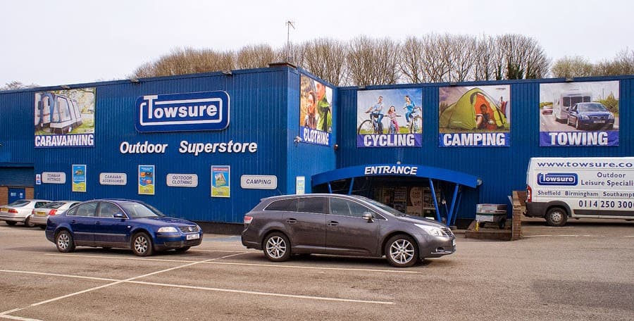 Blue building with large signs for cycling, camping, and towing; parked cars in front and entrance visible.