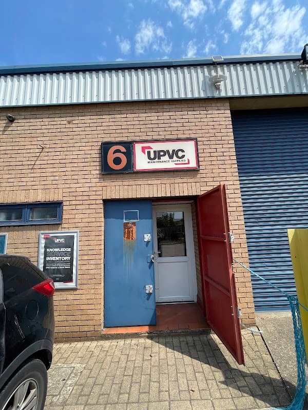 Sign for UPVC Maintenance Supplies on a brick building with a blue door and a red open door, surrounded by a paved area.