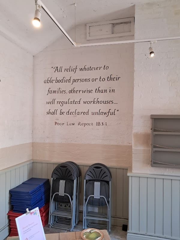 Text on wall quotes Poor Law Report 1834; stacked chairs and tables visible in a bright, airy car park space.