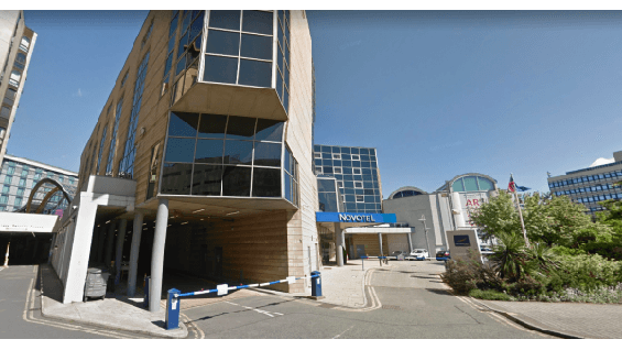 Pay & Display parking area near Novotel in Sheffield, featuring modern buildings and clear blue skies.