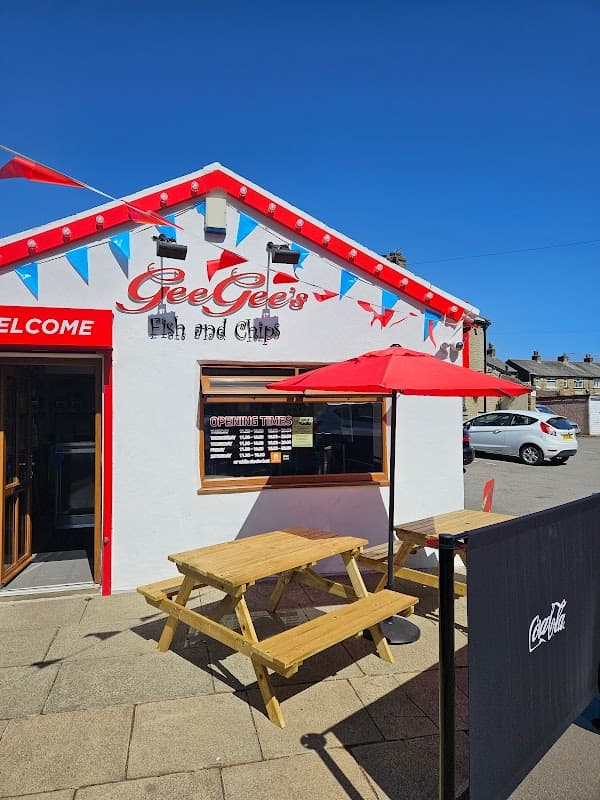 Exterior of Gee Gee's Fish and Chips, featuring a red and white building, outdoor seating, and colorful bunting.