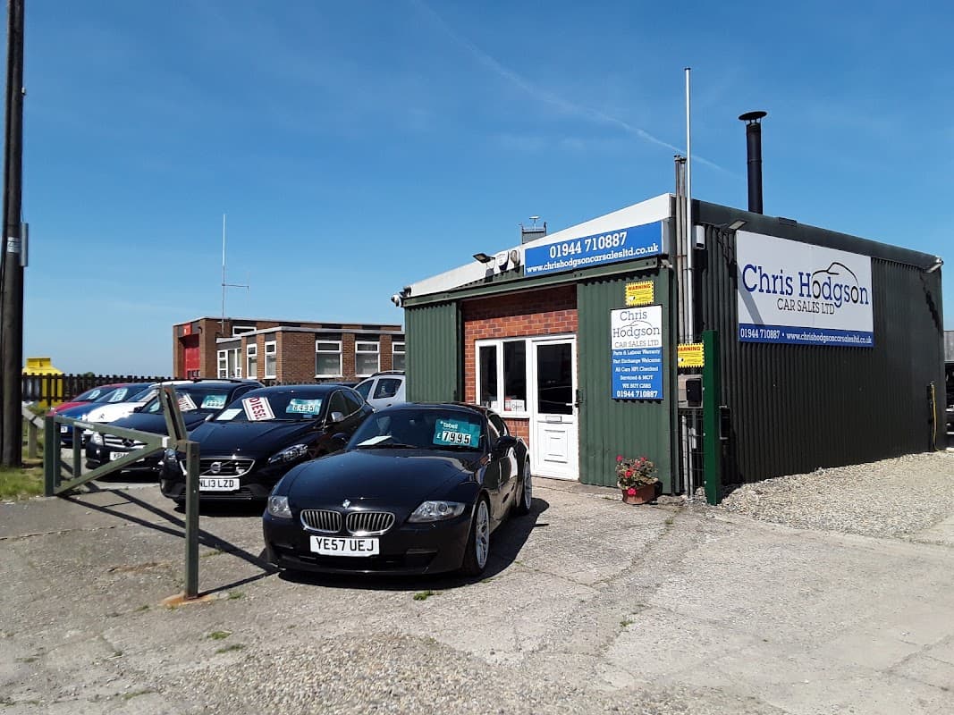 Chris Hodgson Car Sales Ltd shop front in Sherburn, Yorkshire, with parked cars and a clear blue sky.
