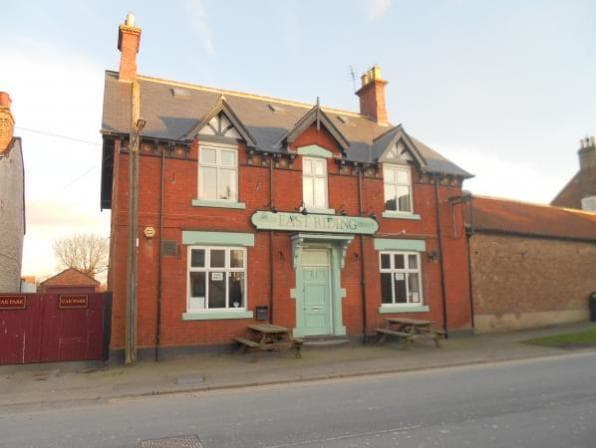 Red brick takeaway with a turquoise sign reading "East Riding," featuring picnic tables outside and a clear blue sky.