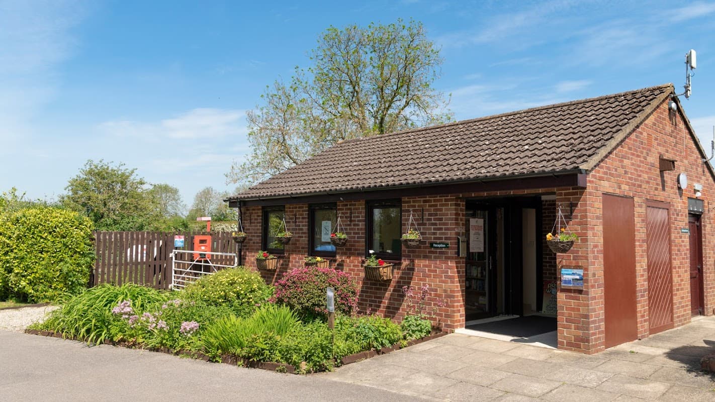 Brick building with a sloped roof, surrounded by green grass and flowering plants, under a clear blue sky.