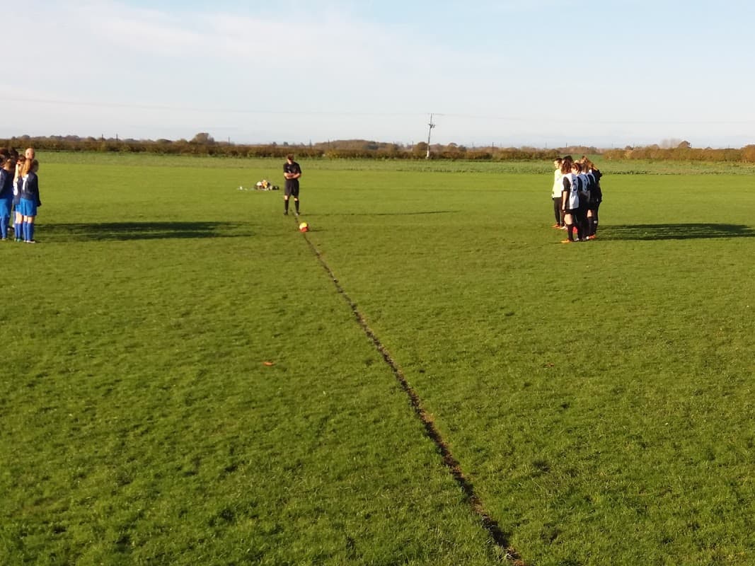 Two teams huddle on a grassy field, preparing for a match under a clear blue sky in Shipton-by-Beningbrough.