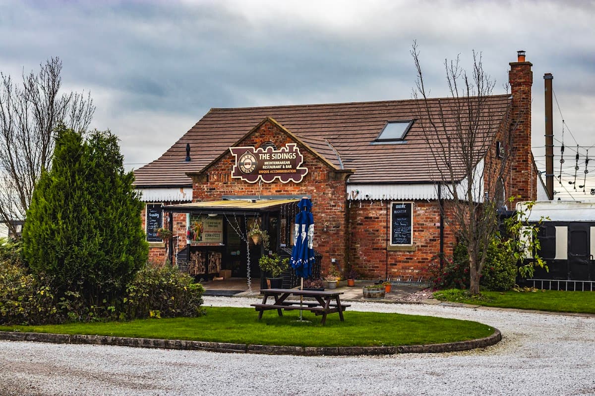 Red-brick building with a sign reading "The Sidings", outdoor seating, and greenery in a rural setting.