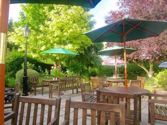 Outdoor seating area with wooden tables and benches, green umbrellas, and lush greenery in a tranquil setting.