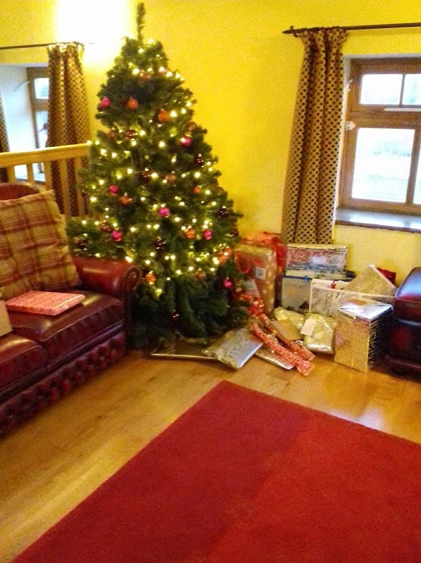 Christmas tree adorned with lights and ornaments, surrounded by wrapped gifts in a cozy interior.